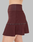 Sidovy av modell i burgundy Iza Performance Skirt, poserar naturligt mot en enfärgad bakgrund, visar kjolens smickrande snitt och längd som är optimal för rörelsefrihet.