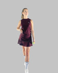 Full kroppsbild av modell klädd i ett matchande sportset med Iza Performance Skirt och en topp i burgundy, poserar på en enfärgad bakgrund, perfekt utrustad för både padel och tennis.