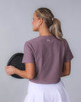 Baksidan av Clara T-shirt – dusty purple ribbad t-shirt för padel, visat med padelrack i handen