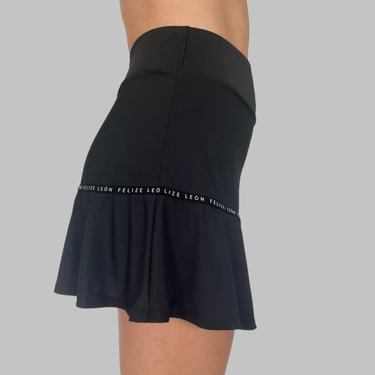 Sidovy av modell i svart Iza Performance Skirt mot enfärgad bakgrund, profilvy som framhäver kjolens slanka linjer och smidiga passform. Padel och tenniskjol med fickor 
