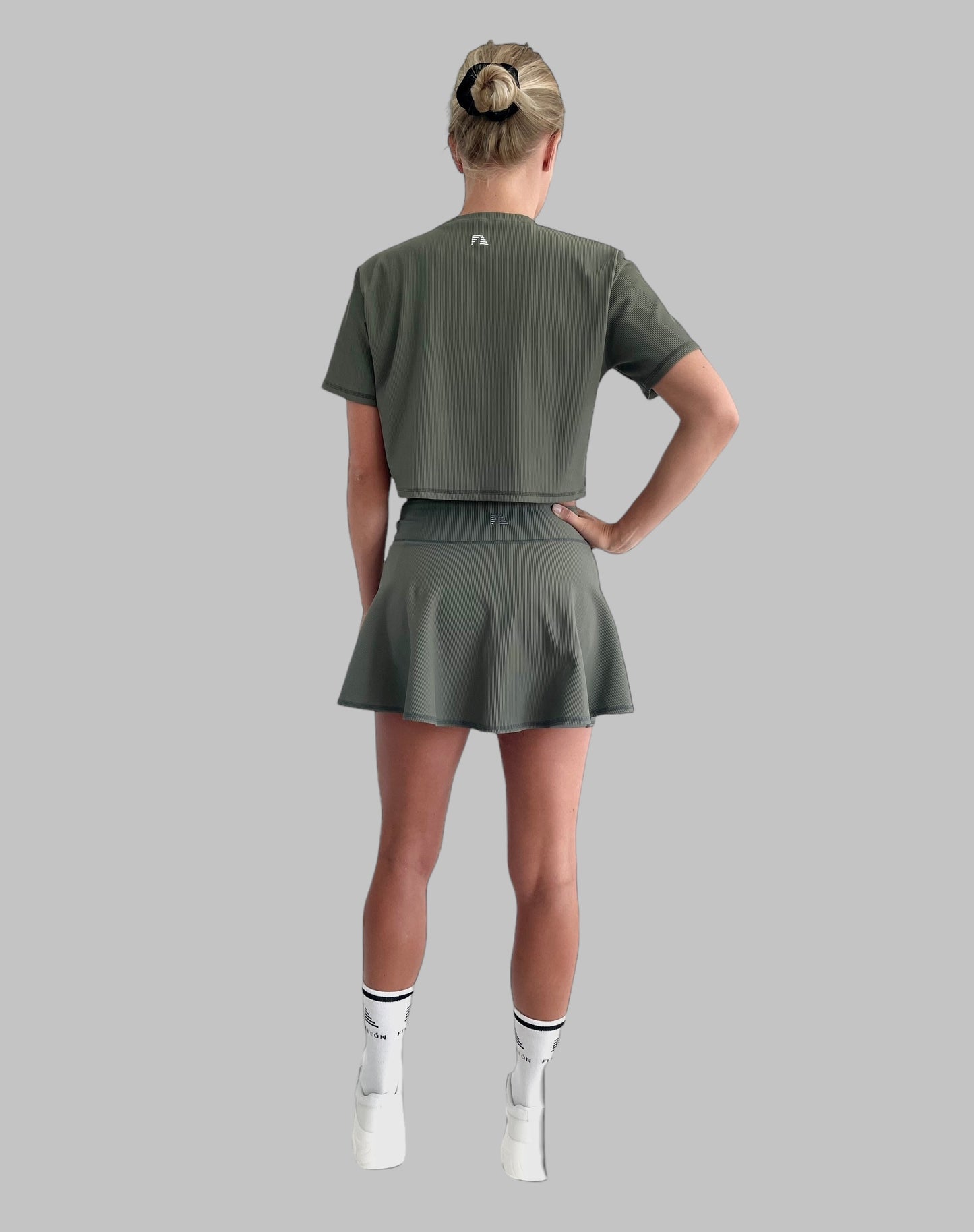 Helkroppsbild bakifrån av en modell klädd i ett matachande grönt set, padelkjol och träningströja i ribbat material. 