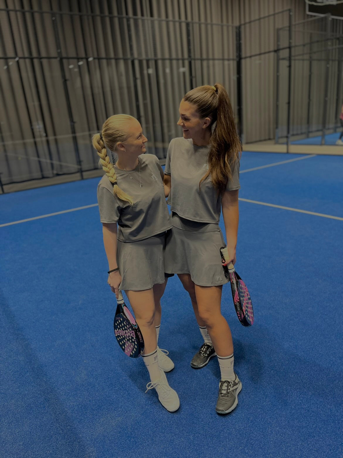 Två kvinnor som står på padelbanan, båda klädda i Zara Classic Cropped T-shirt i grått, redo för en match med komfort och stil.